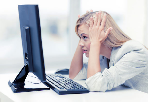 Zoufalá mladá žena s blond vlasy hledí na monitor počítače.